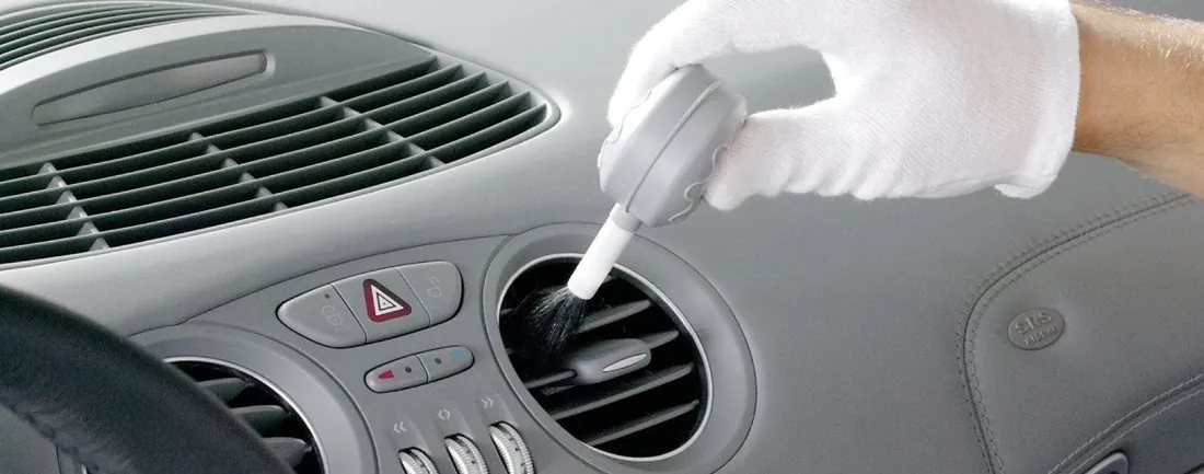 Gloved hand brushing dust out of a dashboard vent